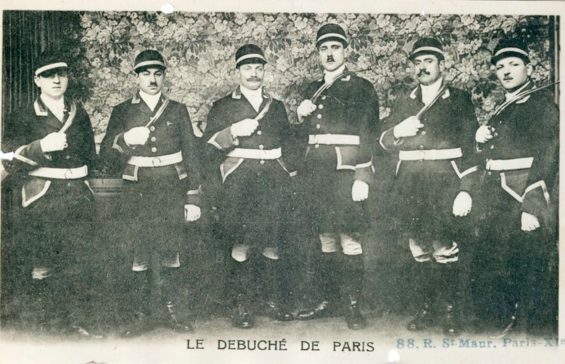 Photographie ancienne : six sonneurs du Débuché de Paris en tenue sombre, trompe à l'épaule, posant en atelier