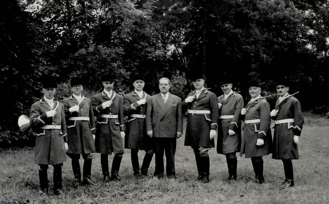 Photographie ancienne : neuf sonneurs alignés en plein air, encadrant un homme en costume