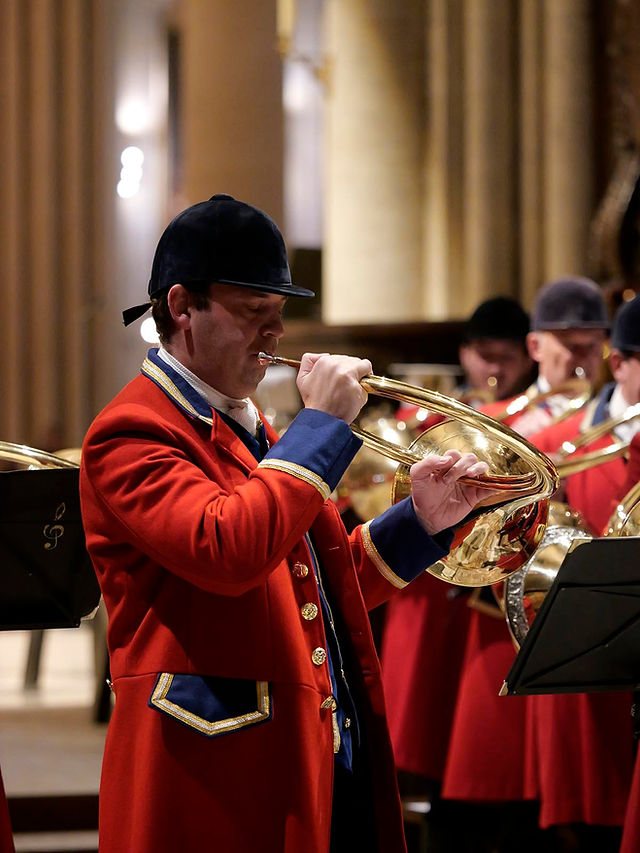 Gros plan sur un sonneur en habit rouge à parements bleus, la trompe posée sur l'épaule, en train de sonner