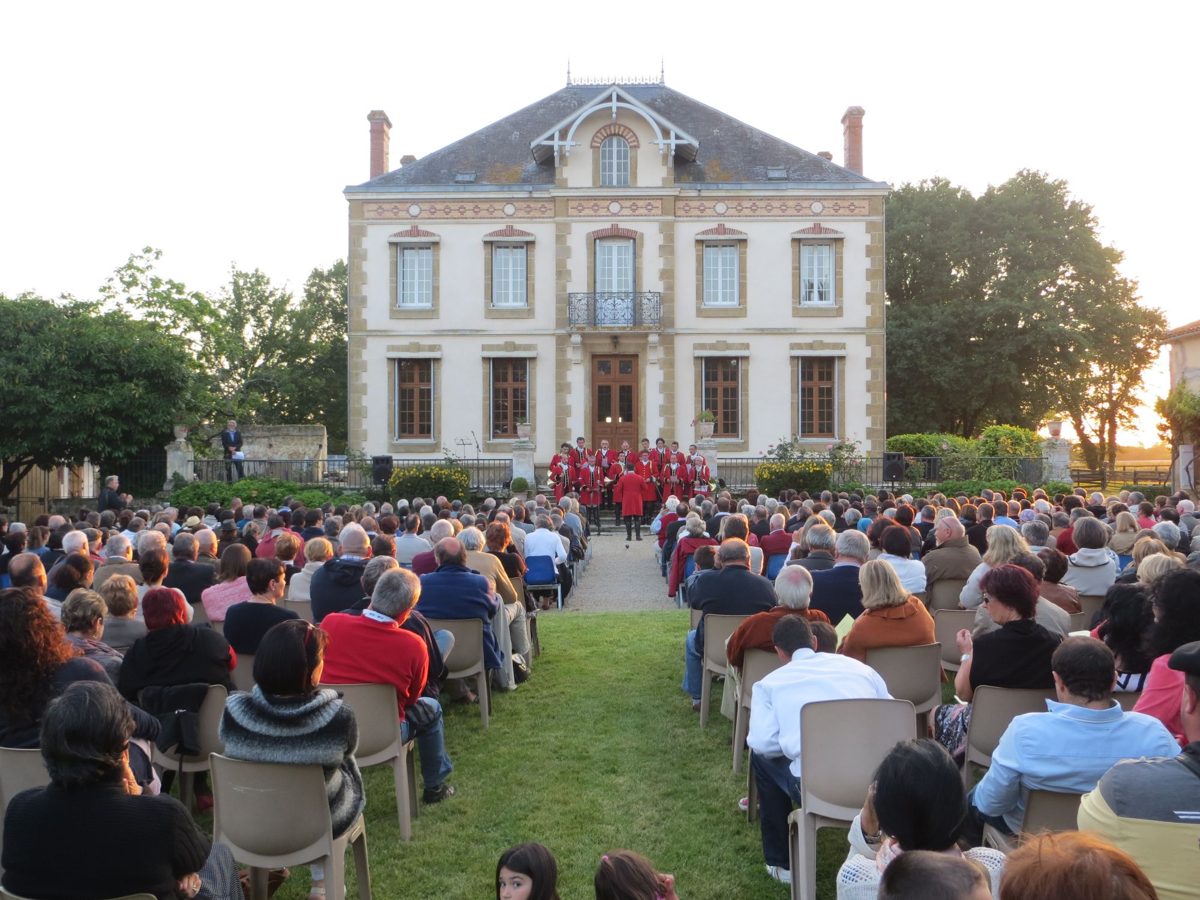 Le public assis dans le parc du château de Watrigant, face aux sonneurs en habit rouge sur le perron