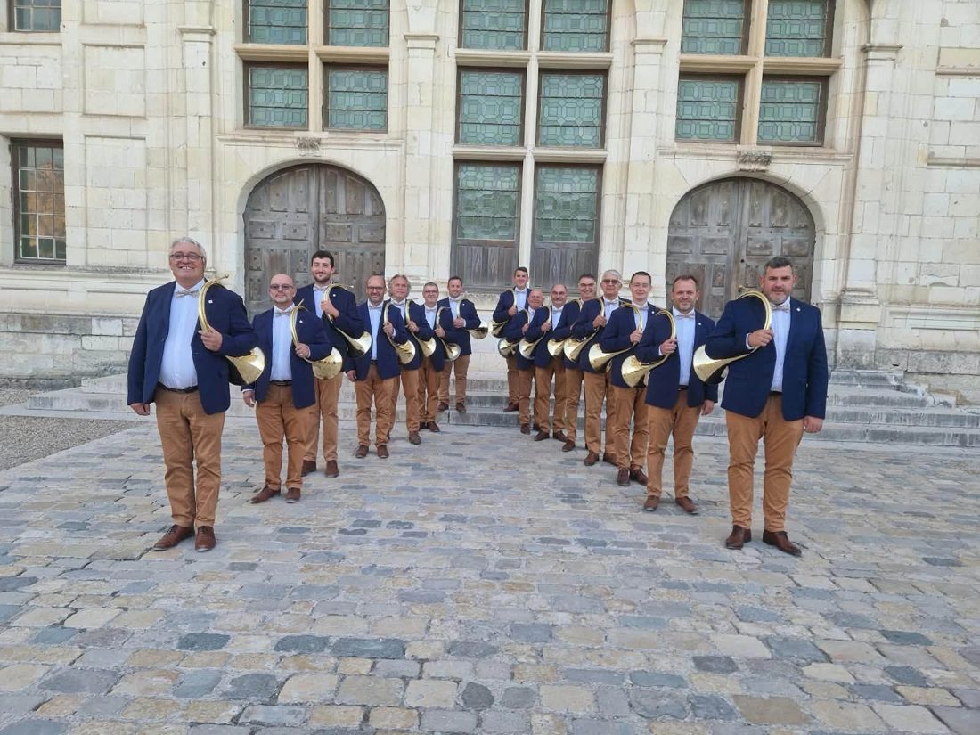 Les sonneurs de Trompe et Fantaisie en veste bleu marine et pantalon camel, trompe à l'épaule, devant la façade d'un château
